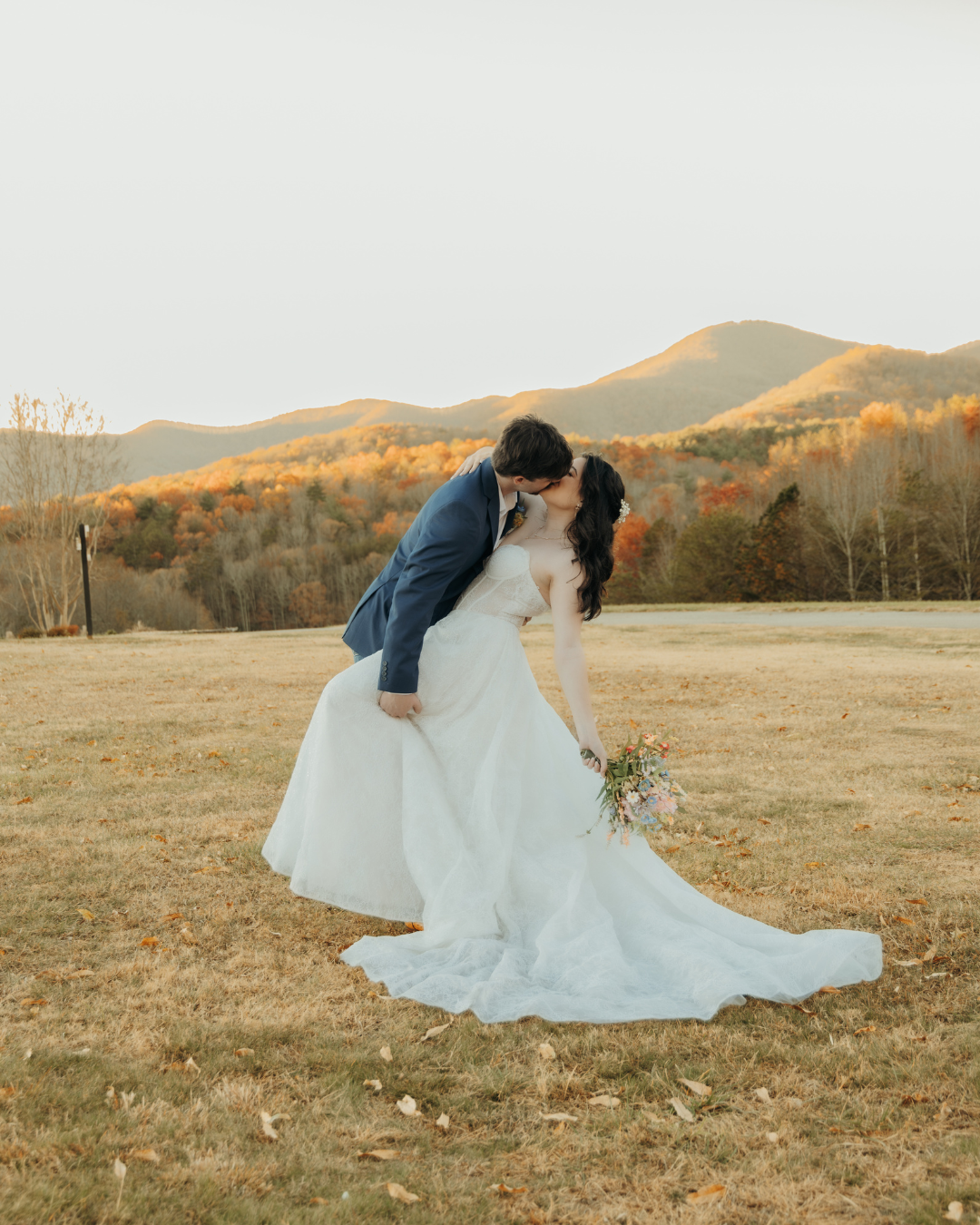 Newlyweds kissing in mountain field during golden hour with fall foliage