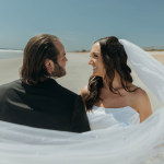 Bride and groom on coastal Georgia beach with flowing veil and clear blue sky