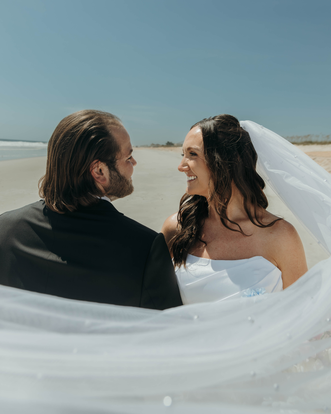 Bride and groom on coastal Georgia beach with flowing veil and clear blue sky