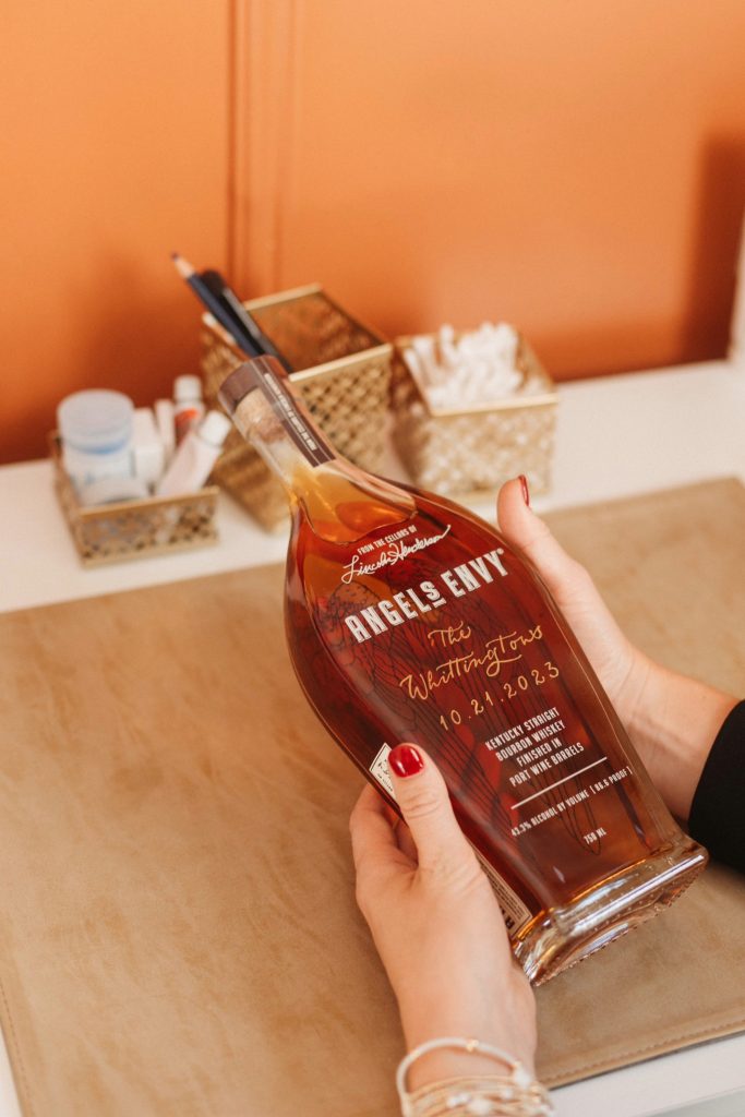 Hands holding custom-engraved Angels Envy bourbon bottle personalized for a wedding celebration