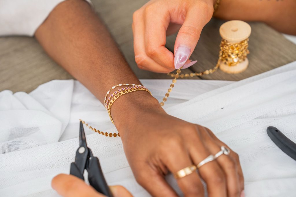 Client wearing stacked gold bracelets and rings while jeweler measures chain from spool for custom fitting