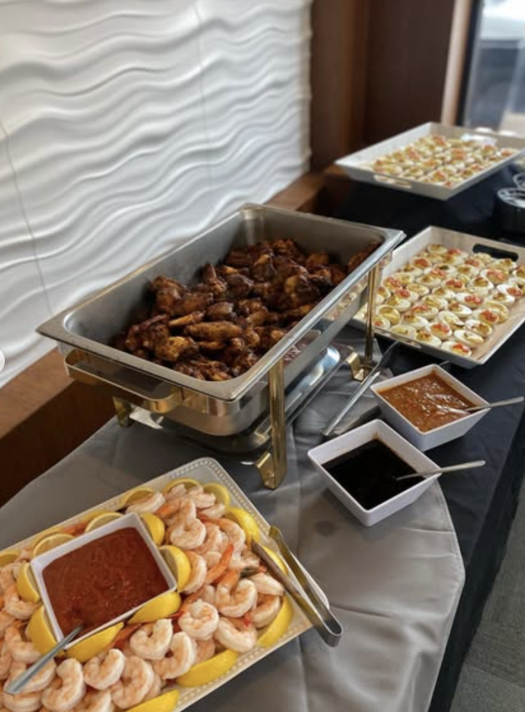 Buffet spread featuring shrimp cocktail, chicken wings, appetizers, and dipping sauces on chafing dishes