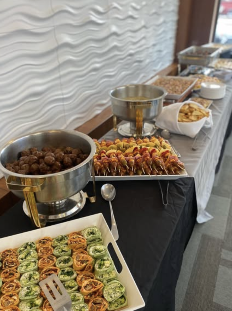 Buffet table spread featuring chafing dishes with meatballs, appetizers, and colorful pinwheel wraps for reception guests