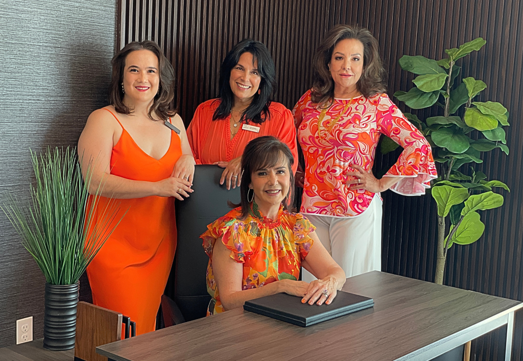 Four KASA real estate agents in vibrant orange and pink attire pose together in modern office setting