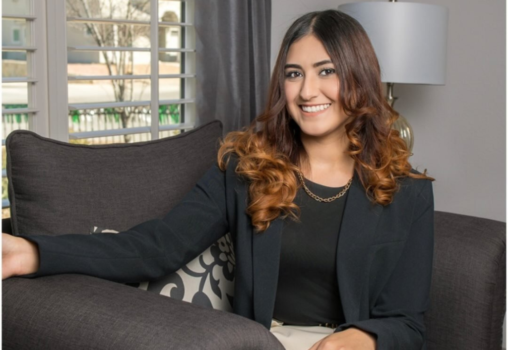 El Paso realtor smiling on gray couch in bright living room with natural light