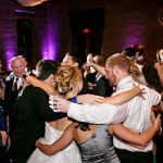 Wedding guests dancing on reception dance floor with purple uplighting and illuminated monogram