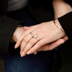 Engaged couple's clasped hands showing princess-cut diamond engagement ring with gold band