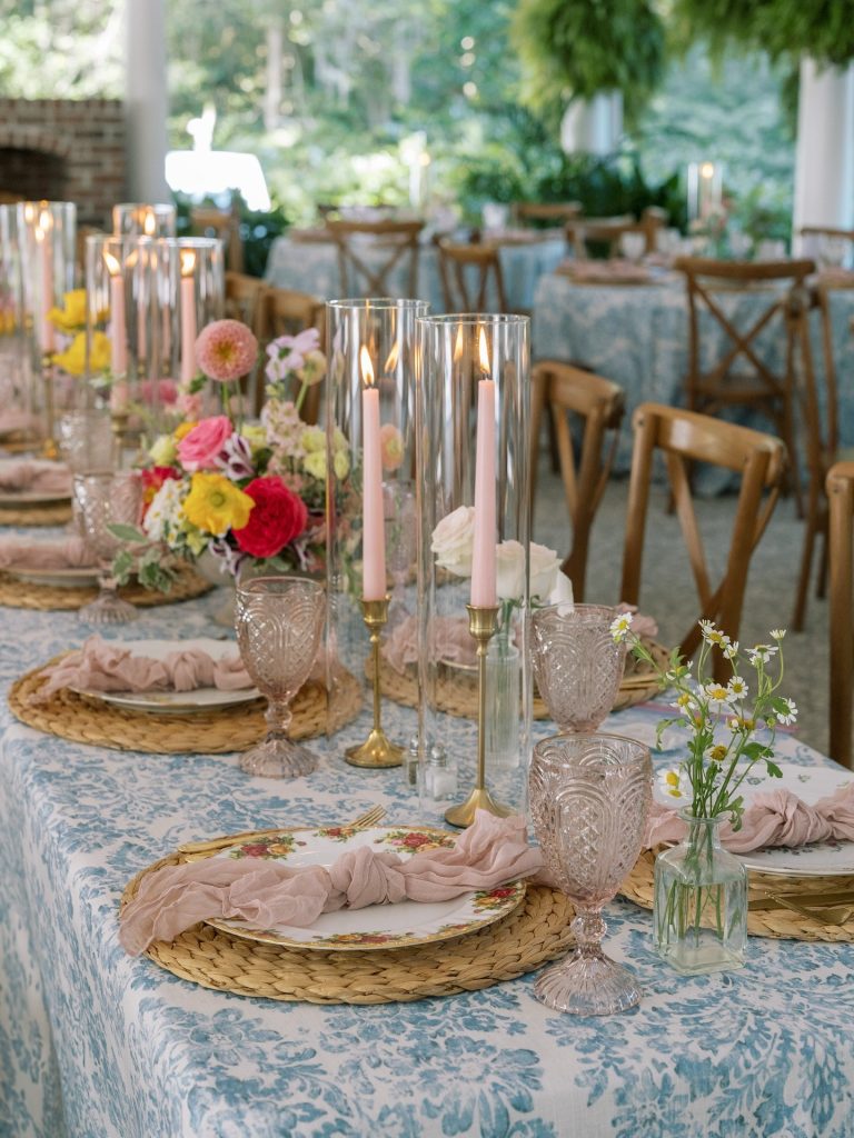 Elegant outdoor wedding reception table with blue floral tablecloth, taper candles, and colorful flower arrangements