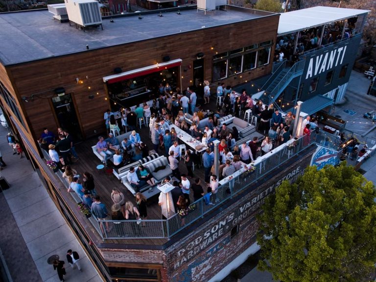 Aerial view of crowded outdoor rooftop wedding reception in Denver with string lights and mountain backdrop