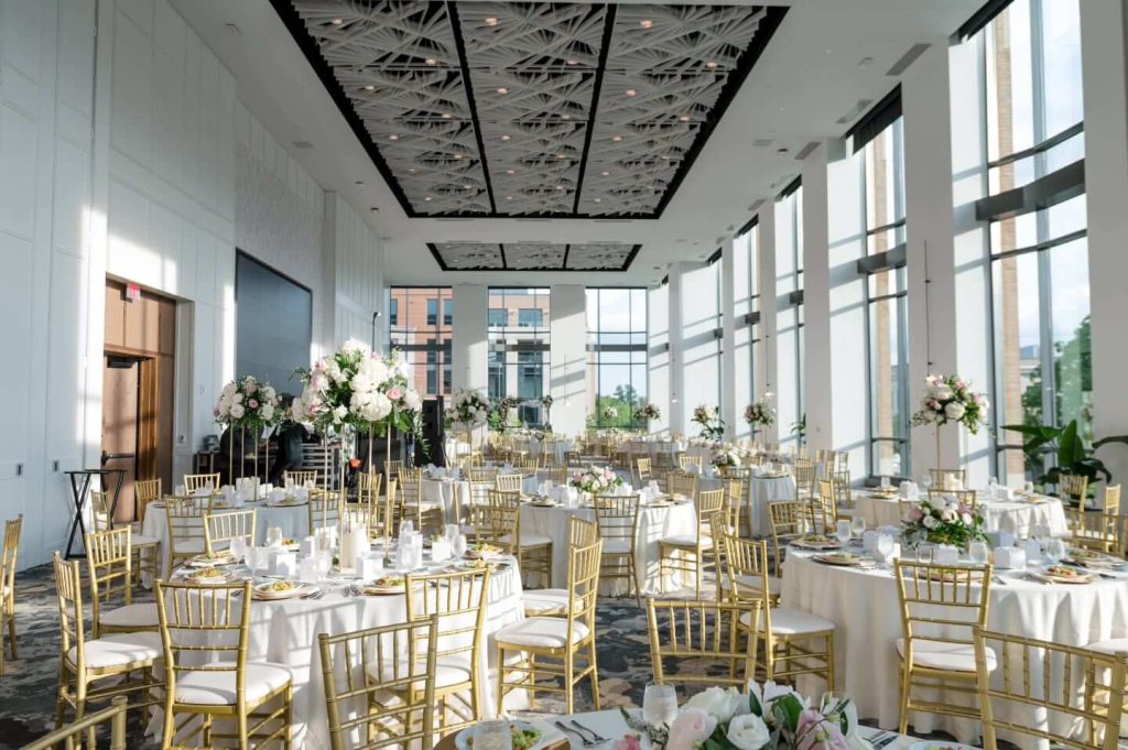 Elegant wedding reception at Vitria on the Square in Columbus, Ohio, featuring round tables with white linens, gold chairs, lush floral centerpieces, and floor-to-ceiling windows overlooking the city.