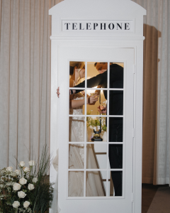 Bride and groom sharing intimate moment inside white vintage telephone booth decorated with flowers