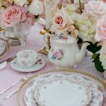 Vintage table setting with pink blooms, floral china teapot, gold-rimmed plates, and pink linens