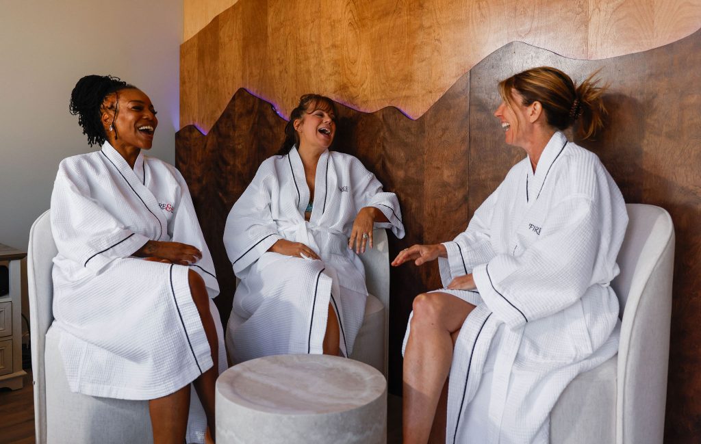 Three women in white robes laughing together in wellness spa lounge