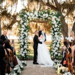 Outdoor wedding ceremony beneath Spanish moss-draped oak trees with white floral arch at The Barn at Covington Farm