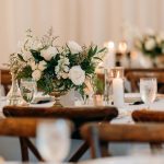 Rustic wooden farm tables with lush floral centerpieces and elegant place settings at barn wedding reception