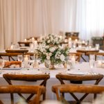 Elegant wedding reception table at The Barn at Covington Farm with white rose centerpiece, pillar candles, and rustic wood chairs against draped backdrop