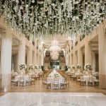 Sophisticated ballroom decorated with suspended flowers, grand staircases, and formal dining arrangement