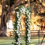 Floral wedding arch adorned with white flowers and greenery beneath a sprawling oak tree