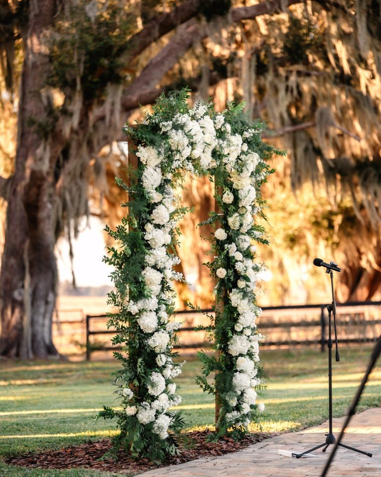 Floral wedding arch adorned with white flowers and greenery beneath a sprawling oak tree