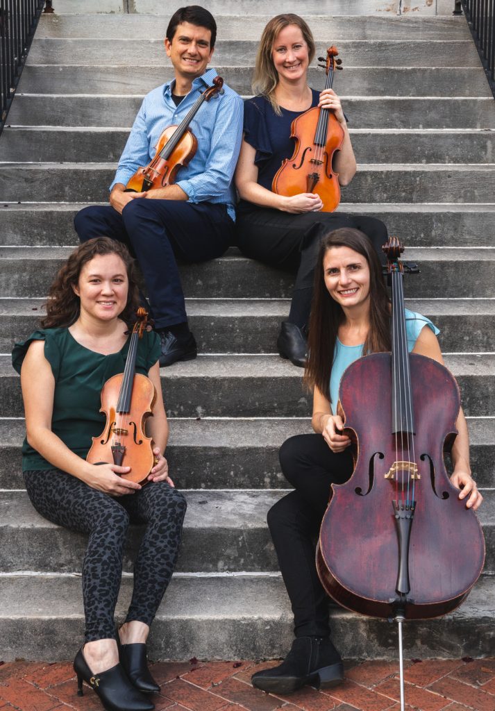 Four string musicians with violins, viola, and cello seated on stone steps