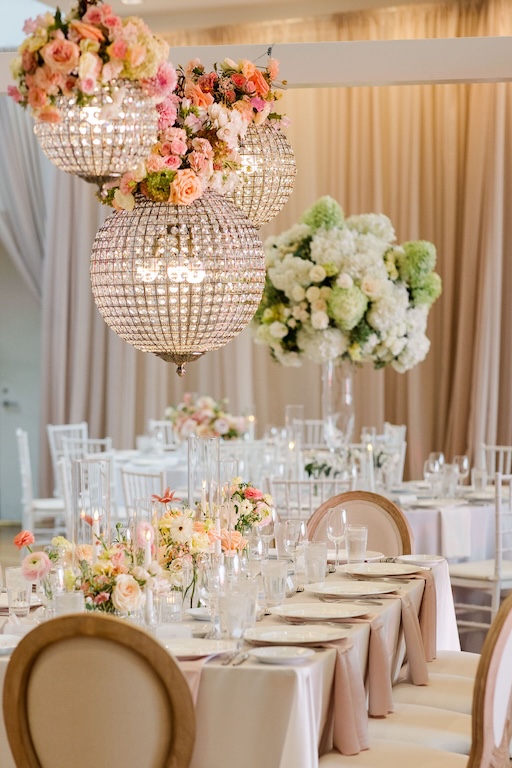 Elegant Columbus wedding reception with blush linens, crystal chandelier installations adorned with pink and peach florals, white and green hydrangea arrangements and romantic floral centerpieces.