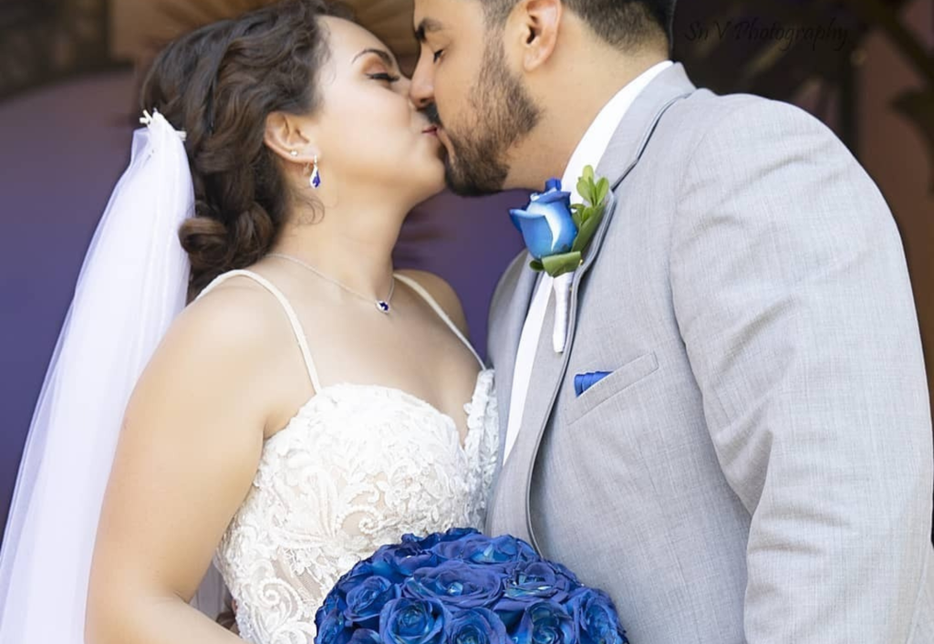 Newlyweds kissing with vibrant blue rose bouquet