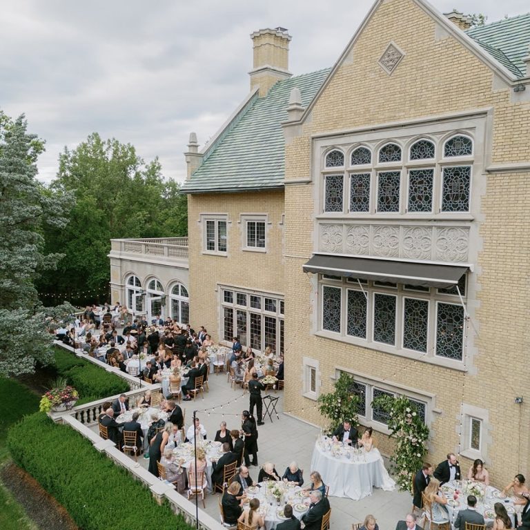 Aerial view of outdoor wedding reception on elegant mansion terrace with guests dining at long tables