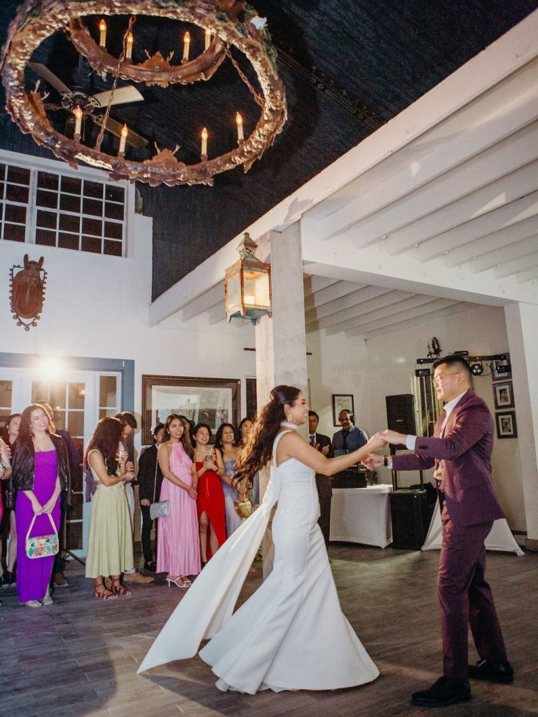 Bride and groom share first dance under rustic chandelier at indoor reception venue