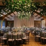 Elegant ballroom reception with sage linens, Chiavari chairs, dramatic greenery chandelier, and neutral draping backdrop