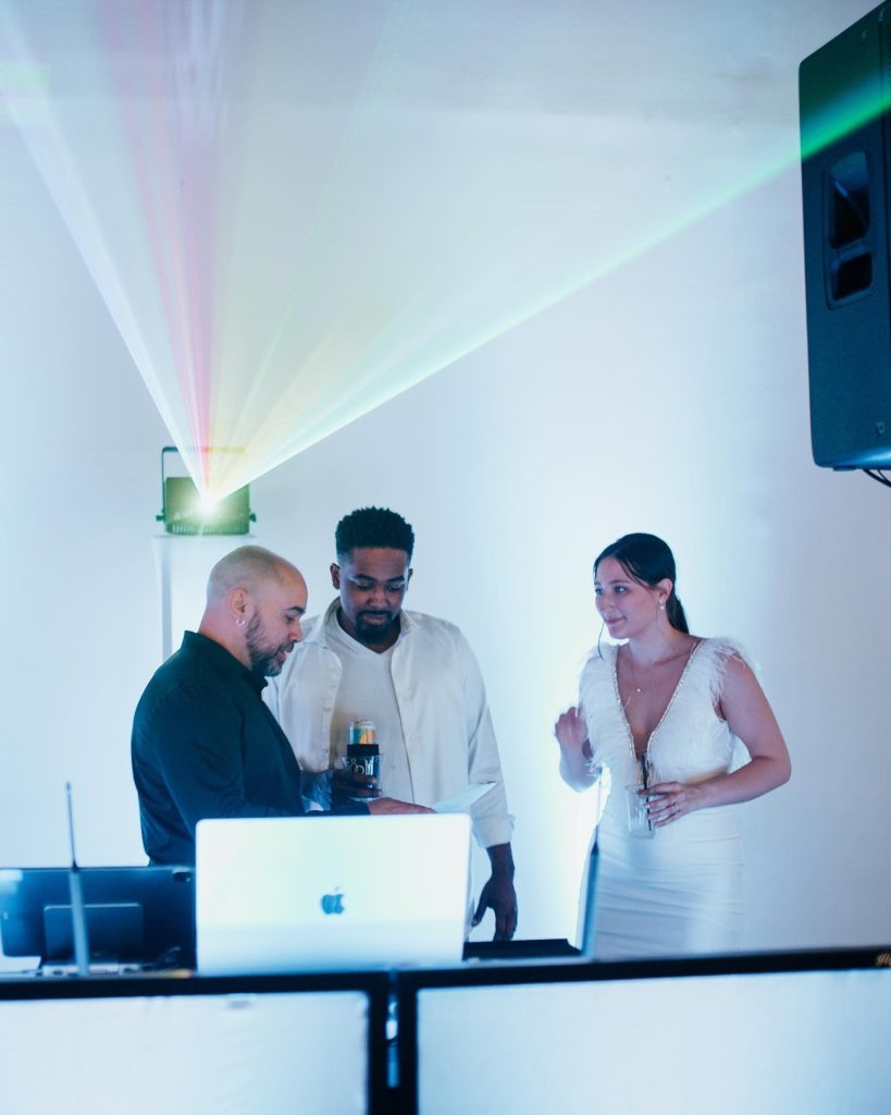 Wedding DJ consulting with bride and groom at setup with laptop and colorful projection lighting