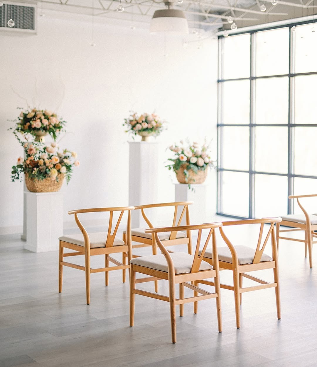 Bright wedding ceremony space featuring wooden chairs and soft floral decor on pedestals