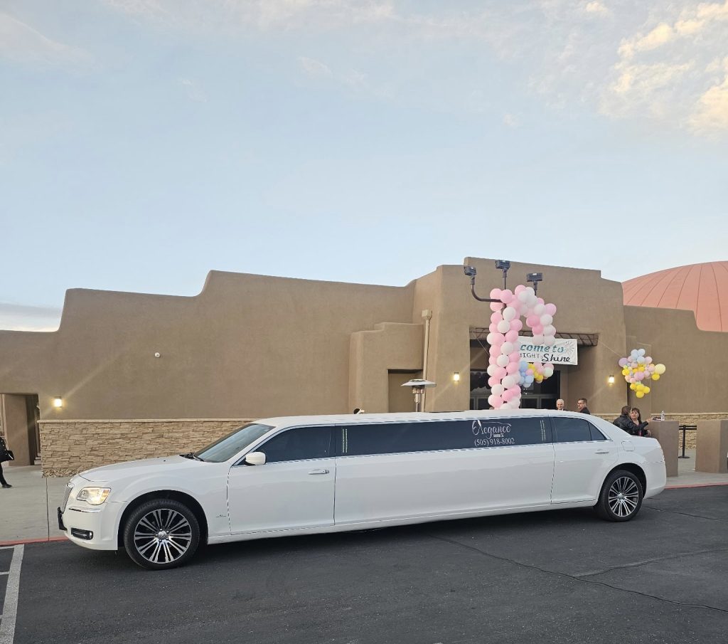 White Chrysler stretch limousine parked outside event venue with pink balloon decorations at dusk
