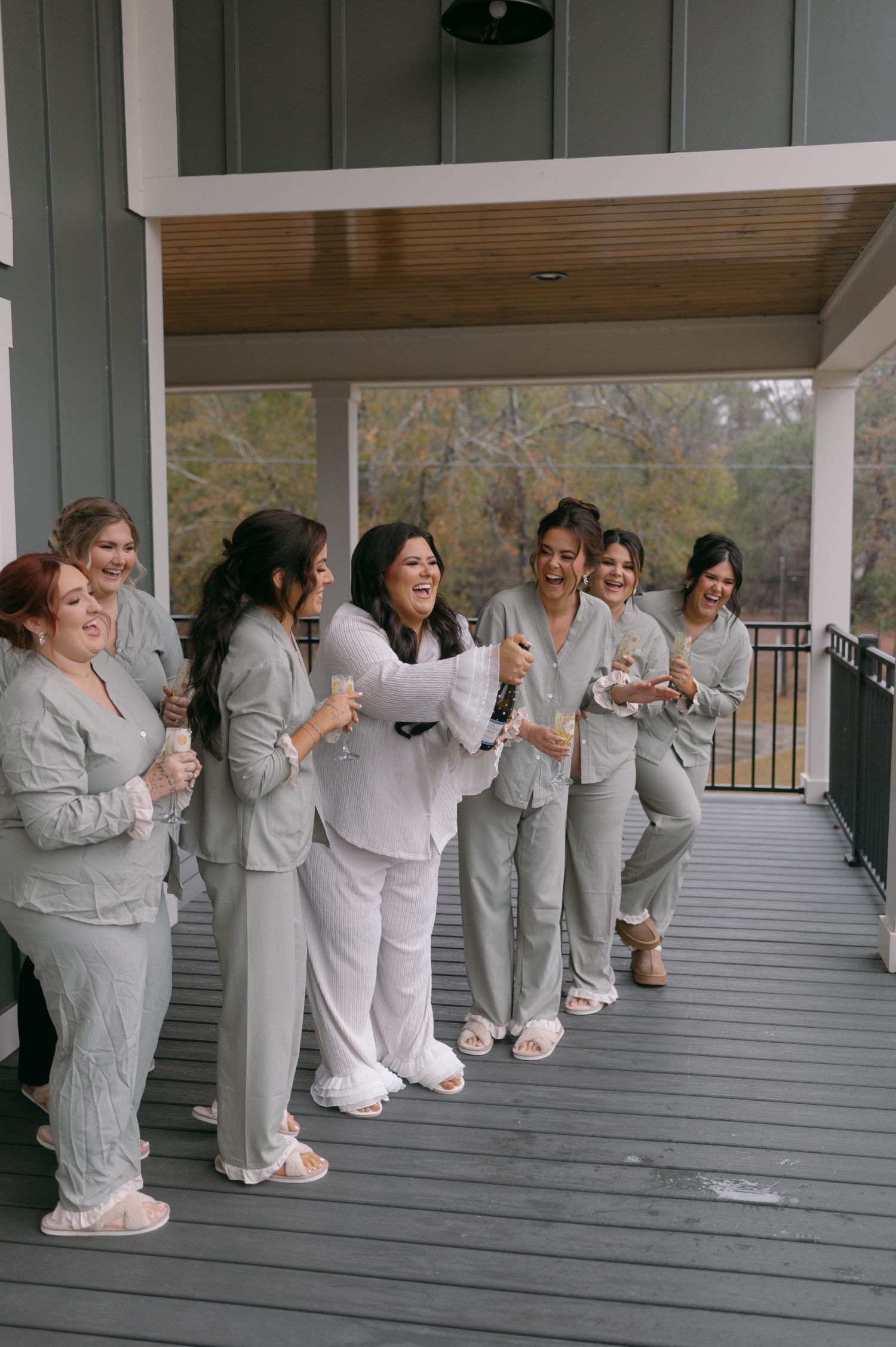 Bridesmaids in matching gray suits sharing a joyful moment on covered porch before wedding ceremony