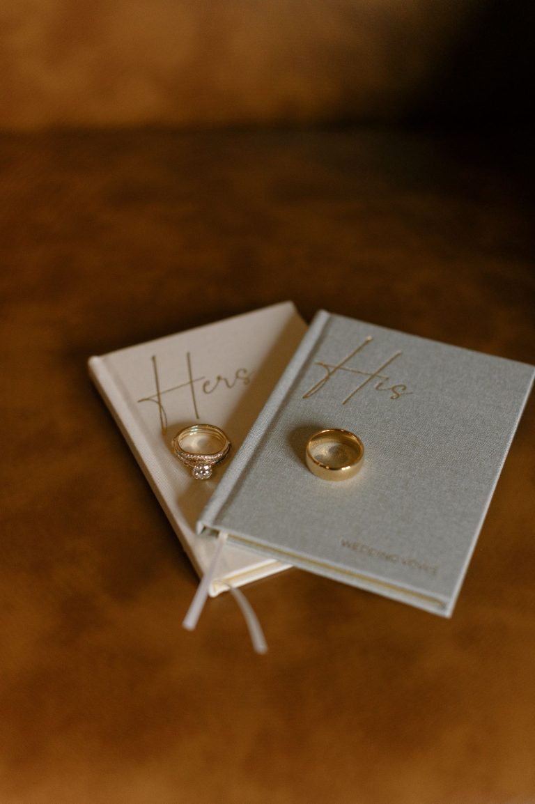 Wedding rings displayed on "Hers" and "His" vow books with gold embossing