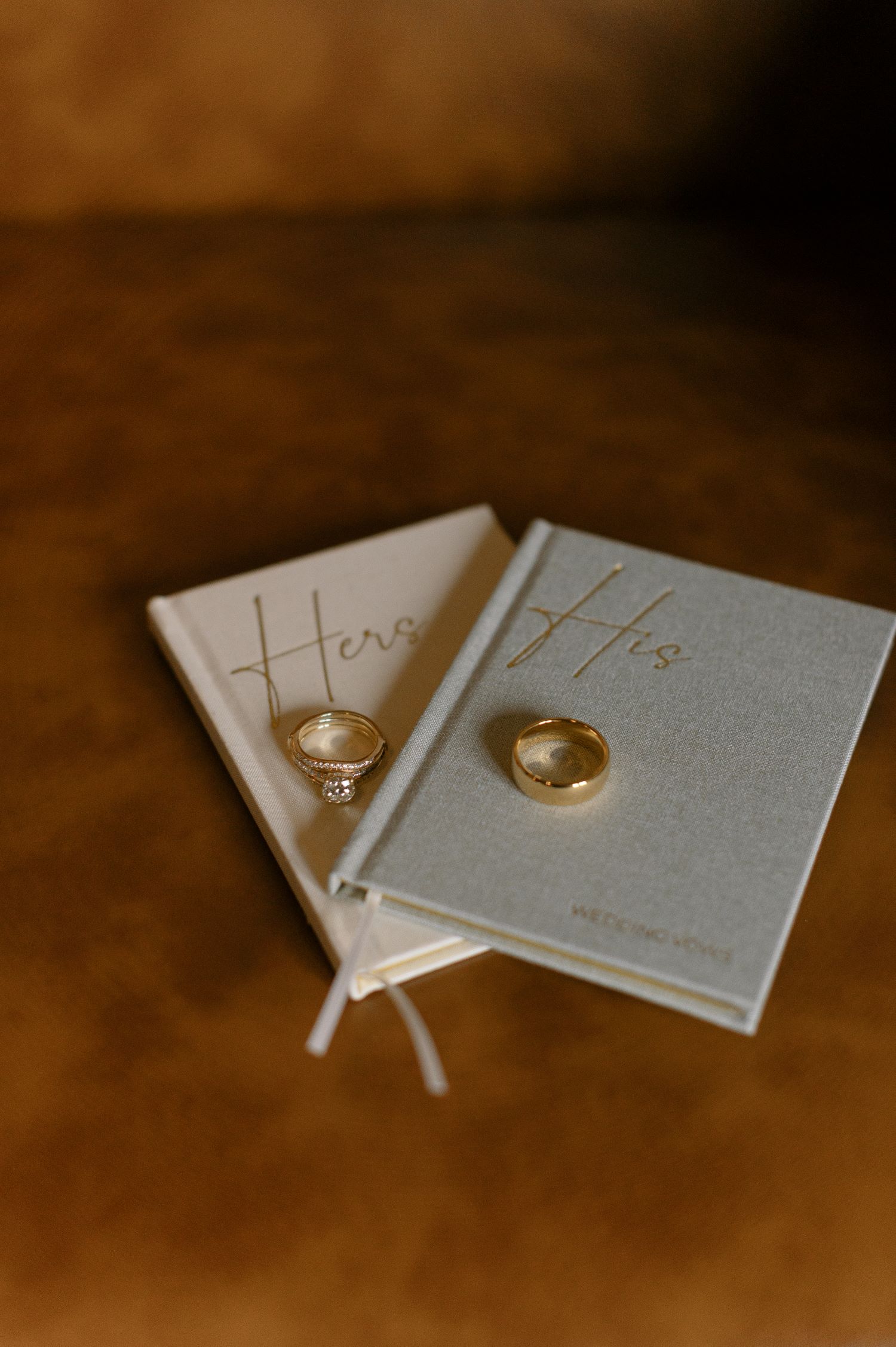 Wedding rings displayed on "Hers" and "His" vow books with gold embossing