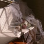 Wedding veil draped over white bridal shoes and floral bouquet in natural window light