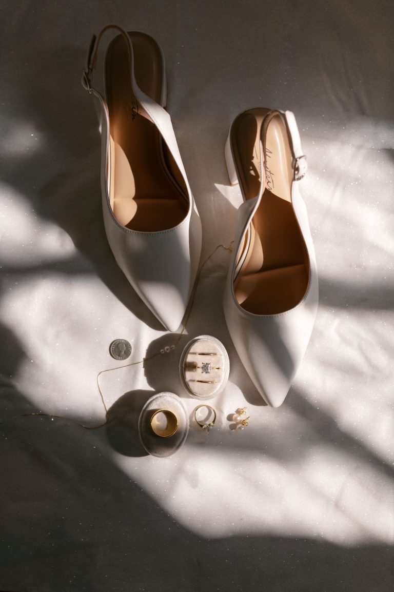 Ivory bridal heels with slingback straps displayed alongside wedding rings, earrings, and jewelry boxes in natural sunlight
