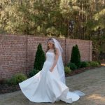 Bride twirling in flowing white wedding gown on brick courtyard with greenery backdrop