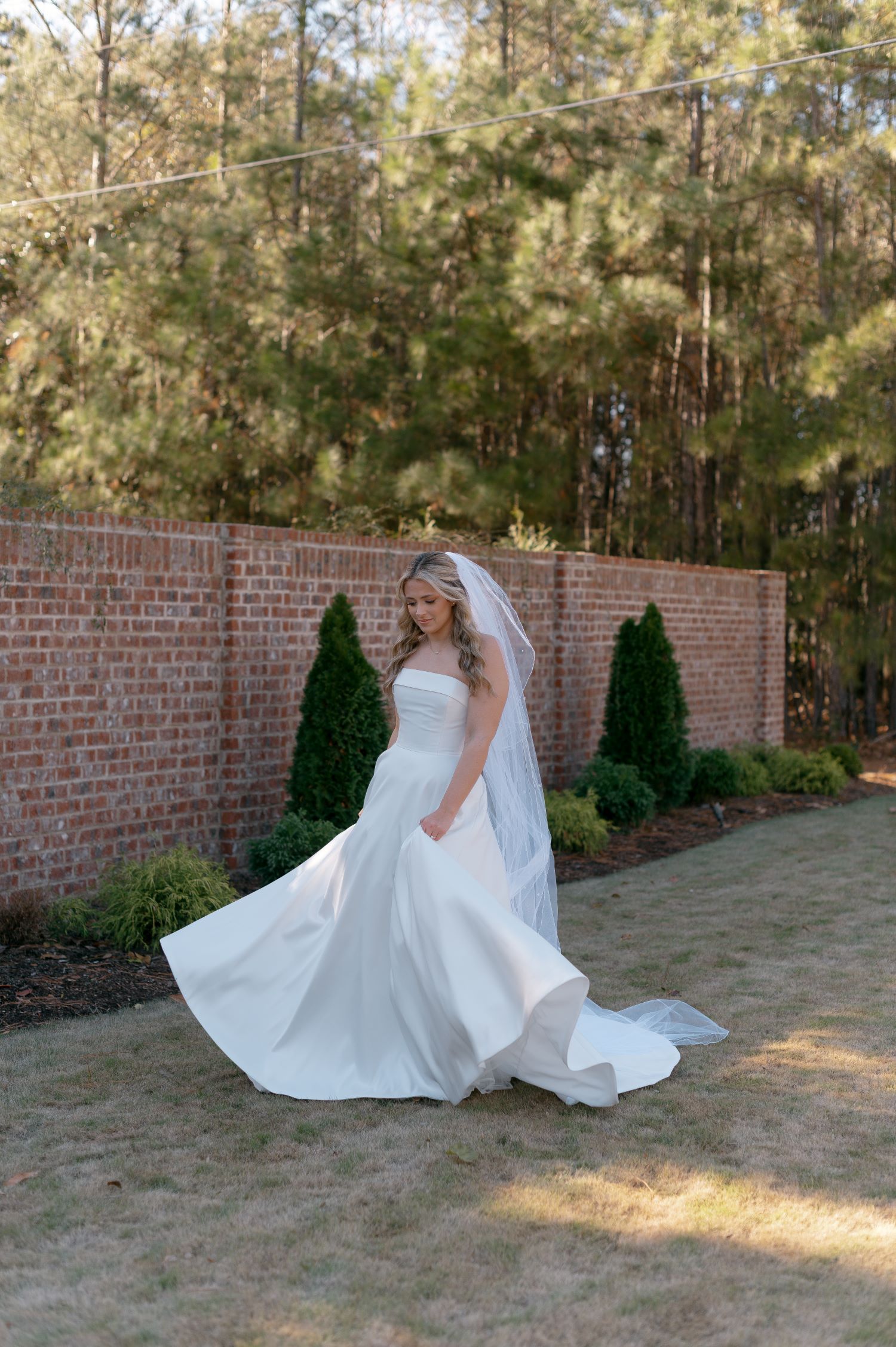 Bride twirling in flowing white wedding gown on brick courtyard with greenery backdrop