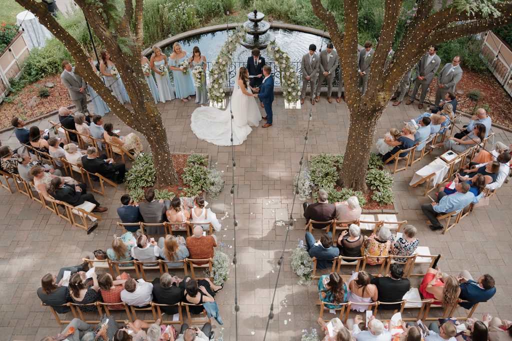 Overhead view of outdoor wedding ceremony with guests seated at tables flanking a center aisle lined with palm trees