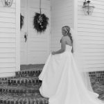 Bride in flowing white ball gown twirling on front porch with wreath-adorned door