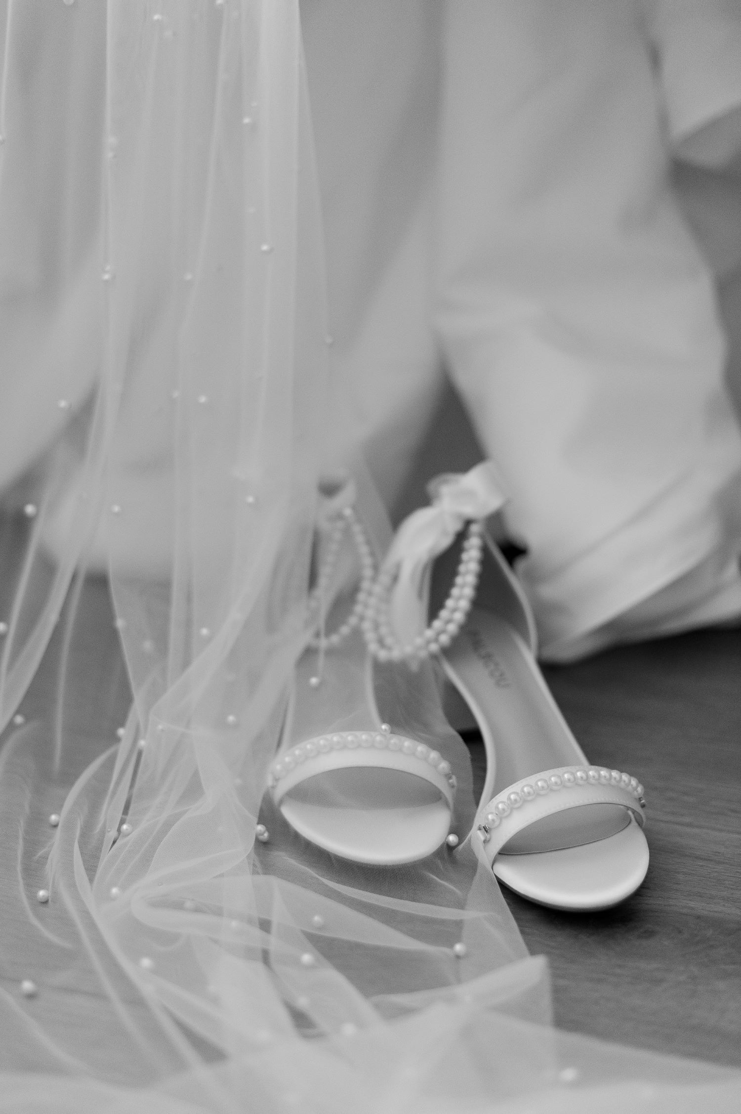 Bride's hands holding white strappy wedding heels with tulle veil in black and white