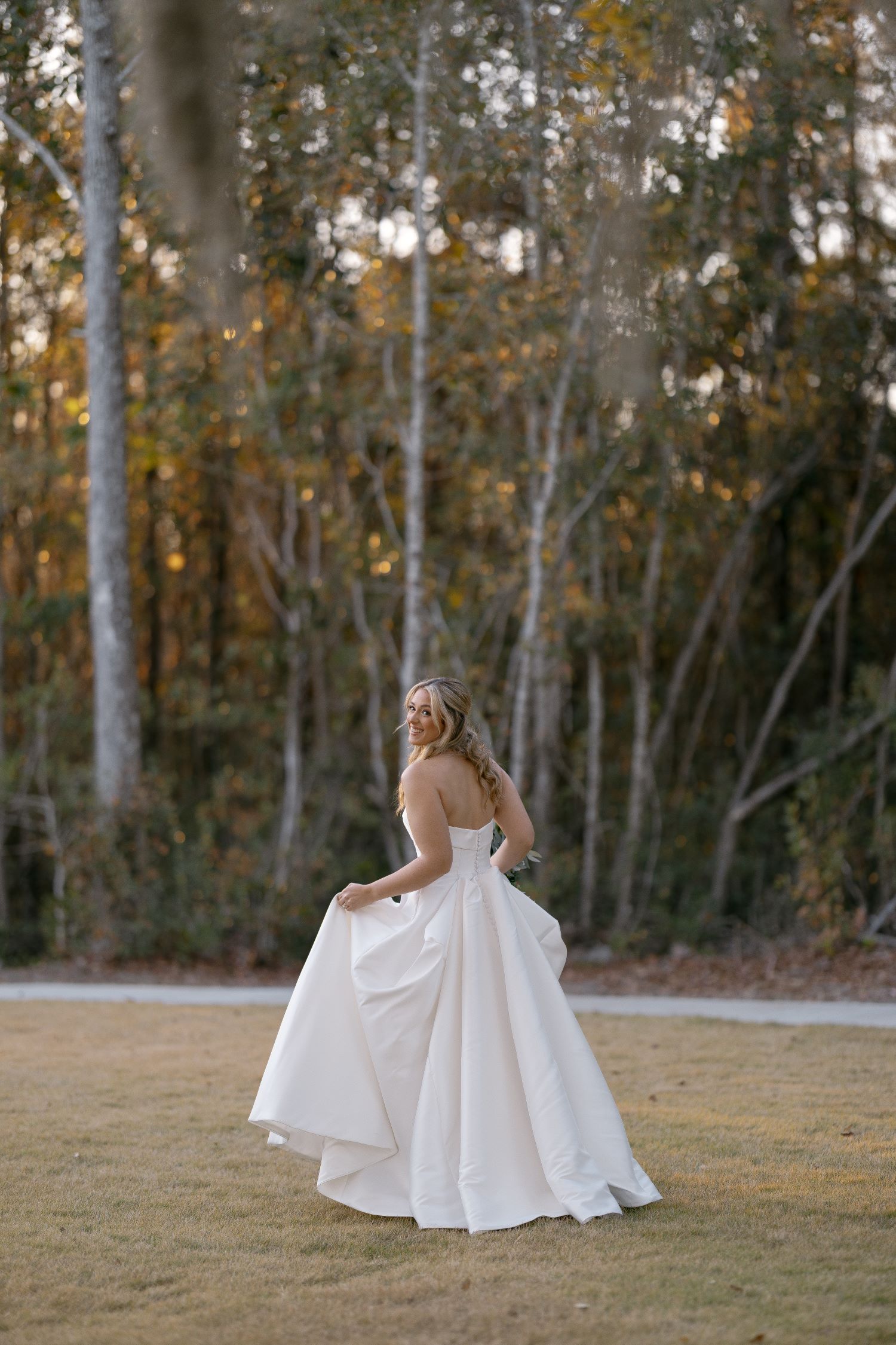 Bride in strapless ballgown twirling outdoors against autumn trees in coastal Georgia