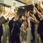 Bride and groom kiss beneath raised white flowers held by their wedding party outside a Columbus wedding venue.