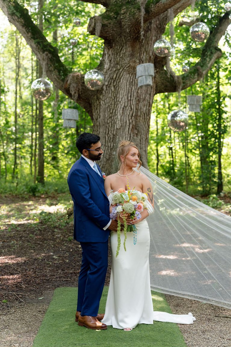 Bride holds a colorful Fiori Florals bouquet with peach, lavender and white blooms beside the groom beneath hanging disco balls.