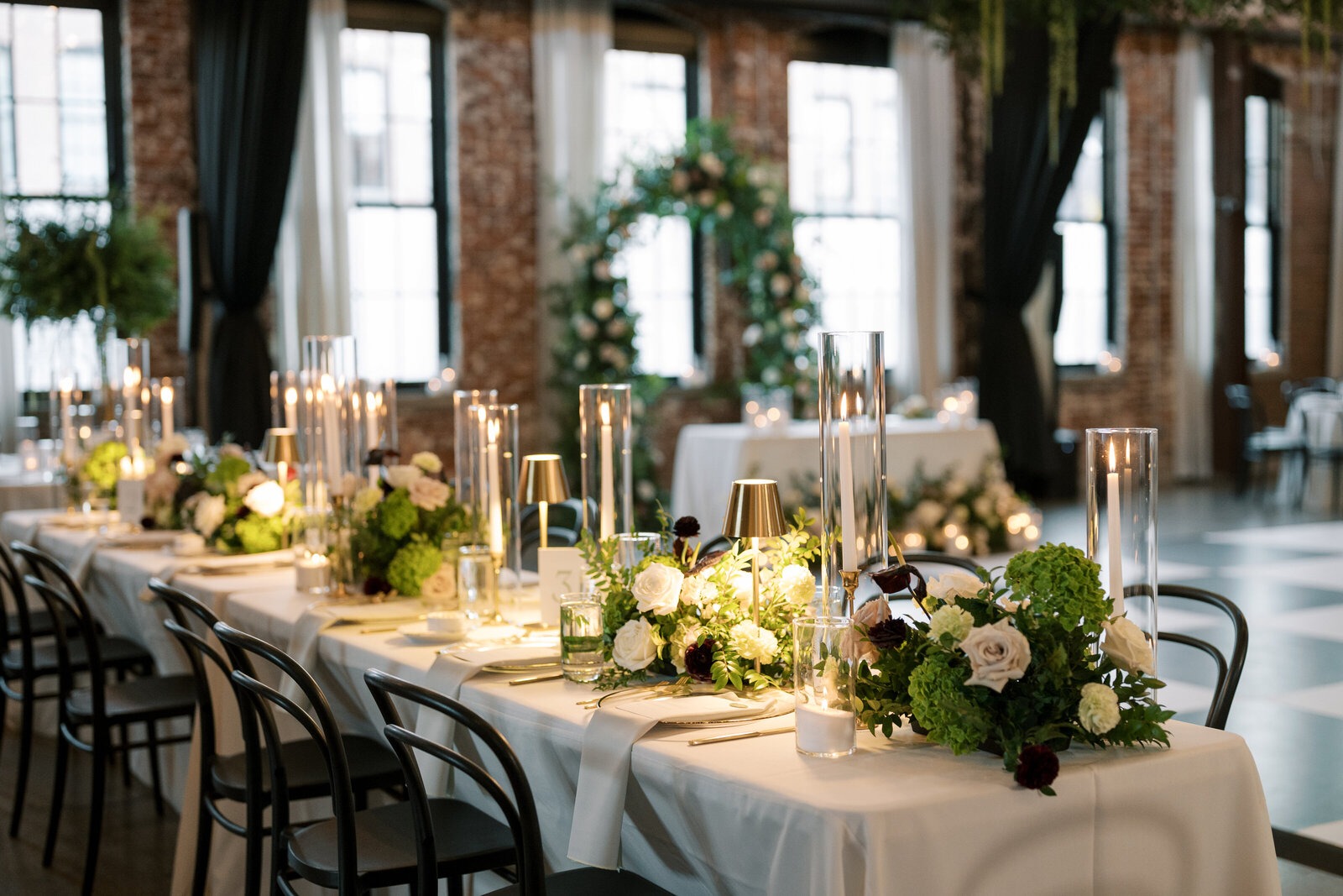 Elegant Columbus wedding reception with lush green and white floral centerpieces, candlelight and modern black chairs.