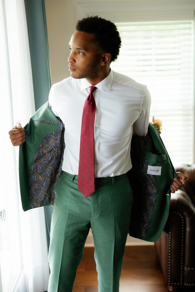 Groom putting on custom emerald green suit jacket with burgundy tie and patterned lining
