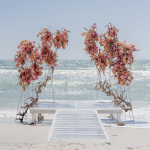 Beach wedding ceremony setup with pink and coral floral arch on white aisle runner overlooking Tampa Bay waters