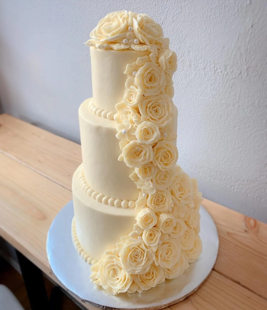 Three-tier ivory wedding cake decorated with cascading cream-colored sugar roses and pearl details