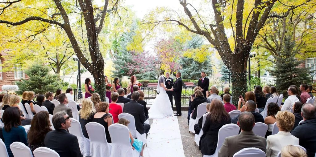 Outdoor wedding ceremony under autumn trees with guests seated on white chairs at Colorado venue